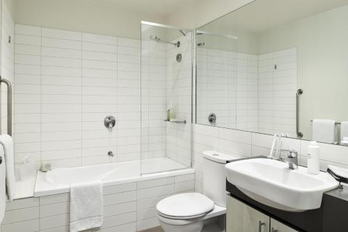 a white bathroom with a tub and a toilet and a sink at Punthill Essendon in Melbourne