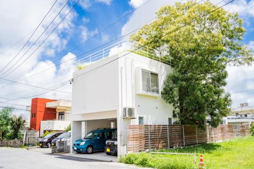 una casa blanca con un coche azul estacionado frente a ella en EM Tree House, en Uruma
