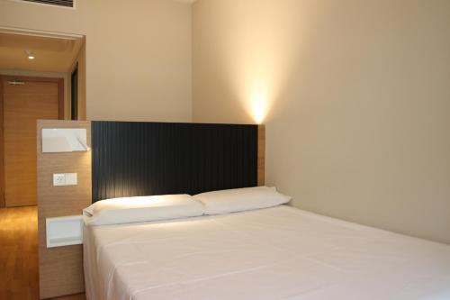 a bedroom with a white bed with a black headboard at Hotel Alcántara in Cáceres