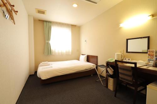 Schlafzimmer mit einem Bett und einem Schreibtisch mit einem Spiegel in der Unterkunft Hotel Green Arbor in Sendai