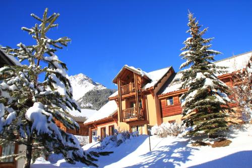 une cabane en rondins dans la neige avec deux arbres dans l'établissement Le Barlèt23 pers Hameau des Chazals Nevache Hautes Alpes, à Névache