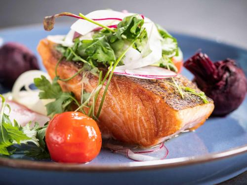 a blue plate with a piece of fish with vegetables on it at The Sebel Melbourne Moonee Ponds in Melbourne