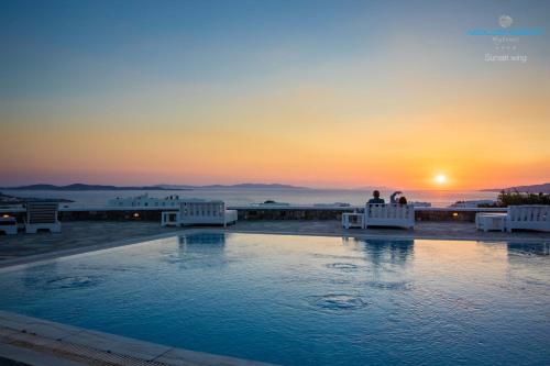 two people sitting on chairs by a pool at sunset at Aeolos Resort in Mikonos