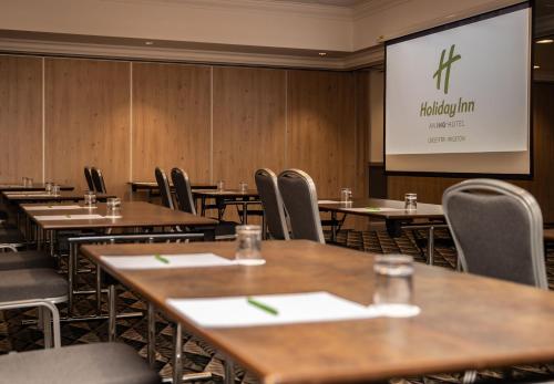 a conference room with tables and chairs and a screen at Holiday Inn - Leicester - Wigston by IHG in Leicester