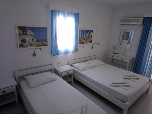 a bedroom with two beds and a window with blue curtains at Nicolas Antiparos in Antiparos