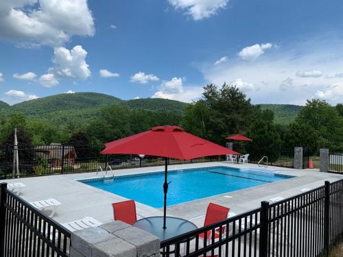 a swimming pool with a red umbrella and chairs at Travelodge by Wyndham Lake George NY in Lake George