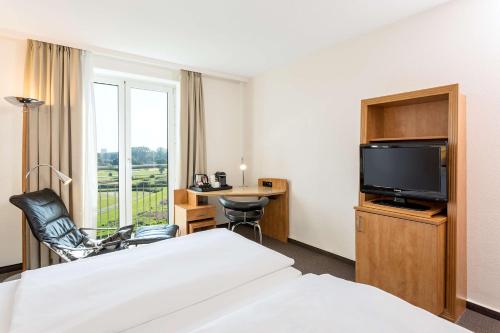 a hotel room with a bed and a tv and a desk at NH Hamburg Horner Rennbahn in Hamburg