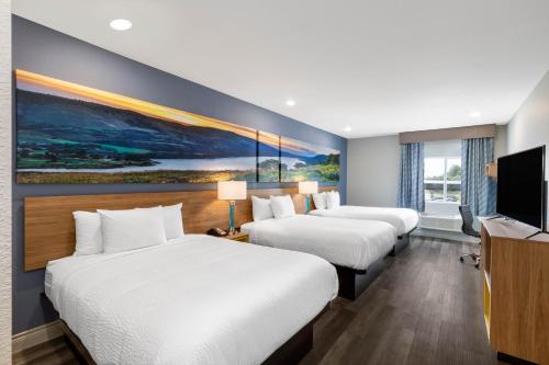a hotel room with three beds and a flat screen tv at Days Inn & Suites by Wyndham Downtown/University of Houston in Houston