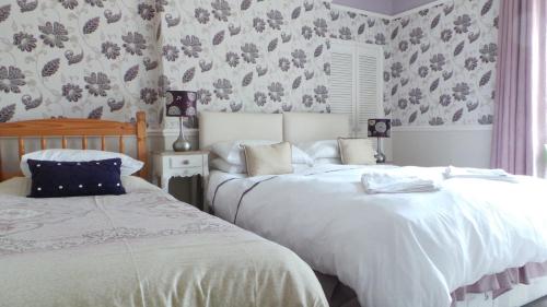 two beds in a bedroom with floral wallpaper at Tynedale Guest House in Penrith