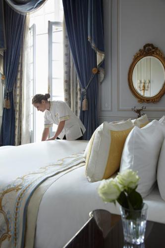 a woman standing in a window near a bed at Shangri-La Paris in Paris