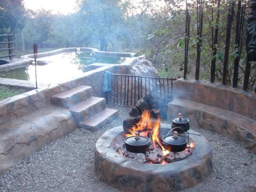 a fire pit with pots and pans in front of a pond at Khaya Umdani Guest Houses in Marloth Park