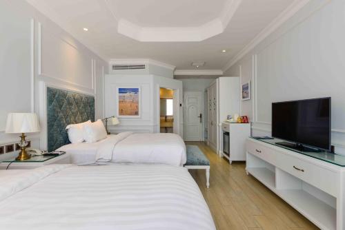 a white bedroom with two beds and a flat screen tv at Lan Rung Beach Resort in Long Hai