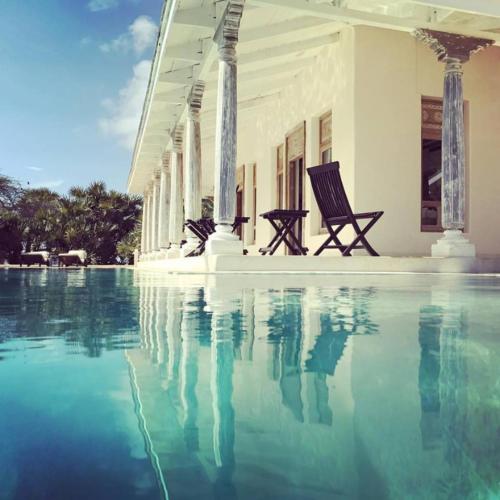 a swimming pool with two chairs in front of a building at The Majlis Resort in Lamu