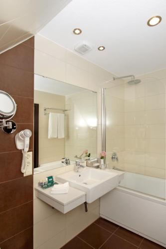 a bathroom with a sink and a tub and a mirror at Grand Palace Hotel Hannover in Hannover