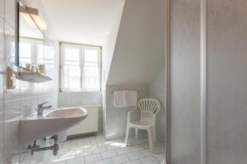a white bathroom with a sink and a chair at Gasthof Siegfried Gruber in Hartmannsdorf