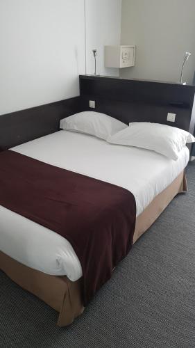 a large bed with white sheets and a brown headboard at Hotel Cosmos in Paris