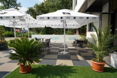 een terras met tafels, witte parasols en planten bij Quartz Boutique Hotel in Mamaia
