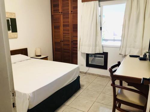a bedroom with a bed and a desk and a window at Flat Amarilis und 110 Riviera de Sao Lourenco SP in Riviera de São Lourenço