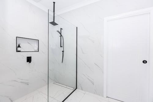 baño blanco con ducha y puerta de cristal en TWO TEN Sleeps 10! Luxury CBD Accommodation, en Wagga Wagga
