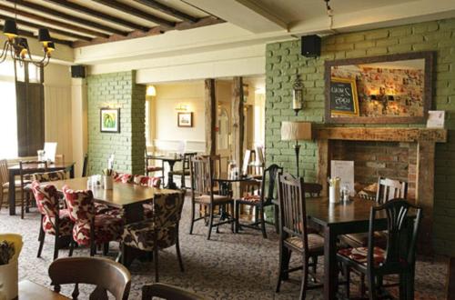 a restaurant with tables and chairs and a fireplace at Raven Hotel by Greene King Inns in Hook