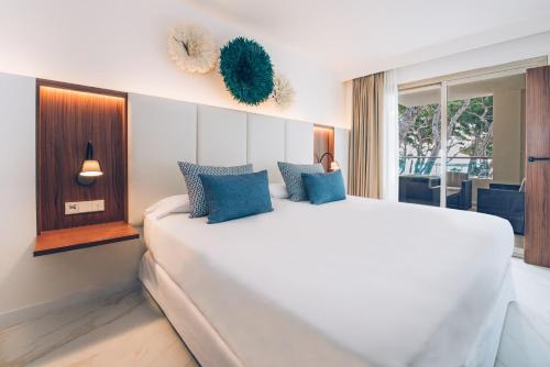 ein Schlafzimmer mit einem großen weißen Bett mit blauen Kissen in der Unterkunft Iberostar Selection Playa de Muro Village in Playa de Muro