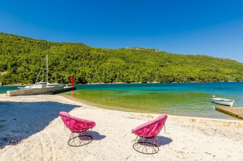 duas cadeiras cor-de-rosa sentadas numa praia perto da água em Holiday Home Barbara em Ston