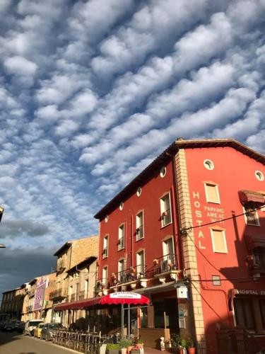 a red building on a street with a cloudy sky at Hostal Delgado in Benabarre