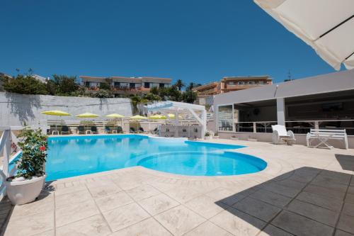 a swimming pool with blue water and umbrellas at Kouros Apartments & Studios By Hotelius in Agios Stefanos