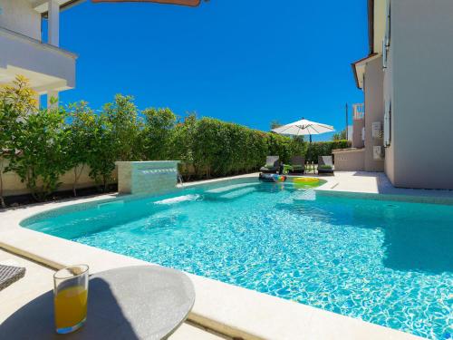 a swimming pool with a glass of orange juice next to a house at Holiday Home Villa Valentina by Interhome in Loborika
