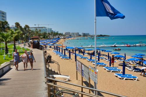 a beach with blue chairs and people walking down a boardwalk at Seafront Protaras Villas in Protaras