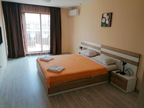 a bedroom with a bed with an orange comforter and a window at Golden Dunes Primorsko Apartments in Primorsko