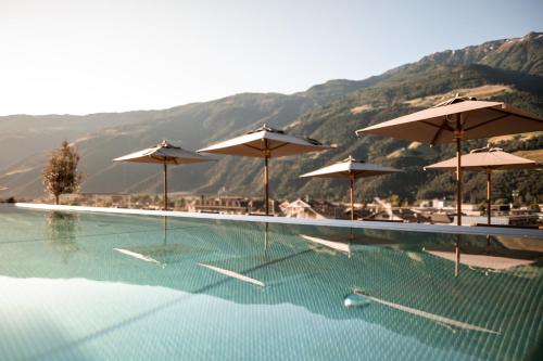 una piscina con sombrillas, mesas y sillas en Sonnen Resort, en Naturno
