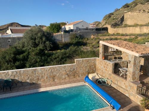 a swimming pool with a stone wall next to a house at Casa Olivia villa in Arboleas