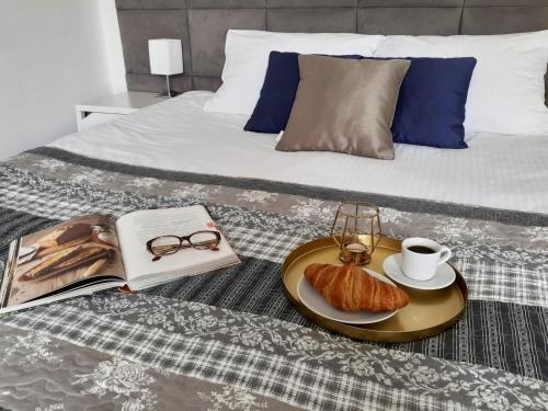 a bed with a tray with a book and a plate of croissants at Vista Residence Premium in Warsaw