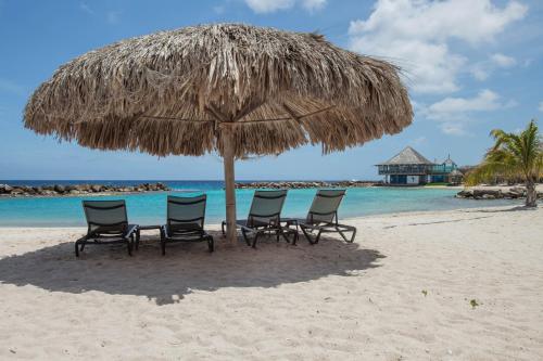 a group of chairs under an umbrella on the beach at Curacao Avila Beach Hotel in Willemstad