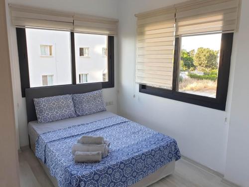 a bedroom with a bed with blue sheets and two windows at Kyrenia Comfort Apartments in Kérynia