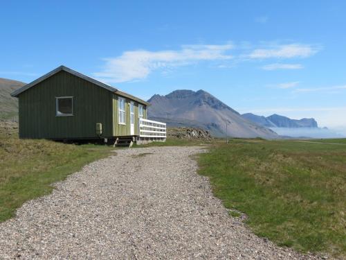 a green house on a gravel road with mountains in the background at Stafafell Cottages in Stafafell