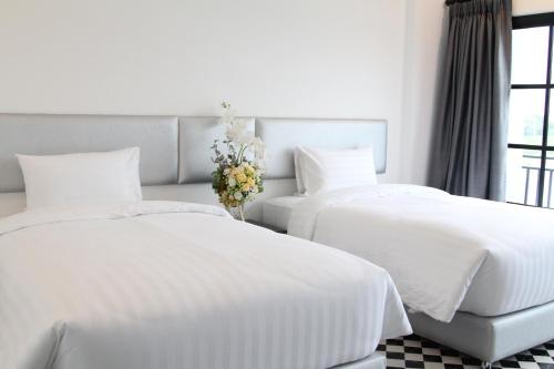 two white beds in a bedroom with a vase of flowers at ESC PARK HOTEL in Pathum Thani