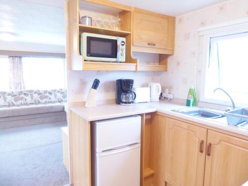 a small kitchen with a sink and a microwave at Beachside, Family-friendly, WiFi, 8 berth Caravan 158 in Ingoldmells