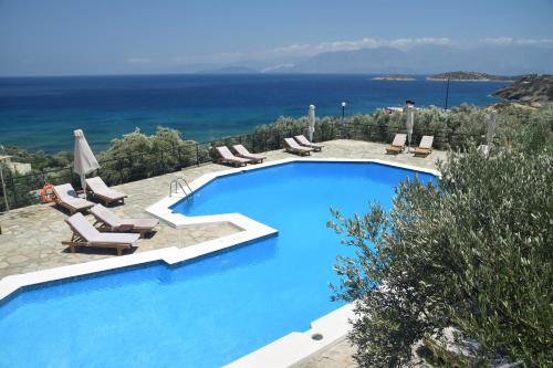 a large blue swimming pool with chairs and the ocean at Meliti Hotel (Adults Only) in Agios Nikolaos