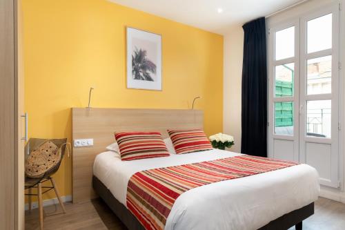 a bedroom with a bed with yellow walls and a window at Hôtel Byakko Nice in Nice