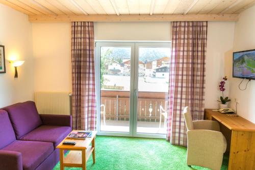 a living room with a purple couch and a balcony at Appartement- und Wellnesshotel Charlotte - 3 Sterne Superior in Seefeld in Tirol