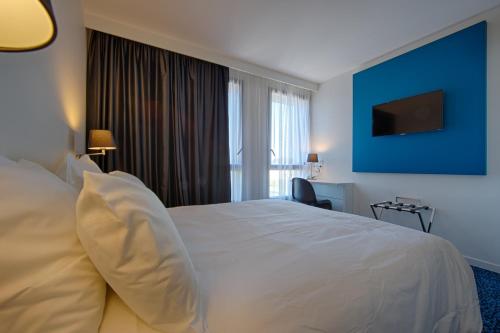 um quarto de hotel com uma cama branca e uma parede azul em Nex Hôtel em Tarbes