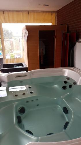 baño con bañera verde y ventana en Het Gildehuis met sauna en jacuzzi, en Stevensweert