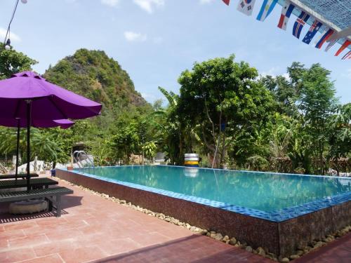 a swimming pool with a purple umbrella and a table at Phong Nha Love Homestay in Phong Nha