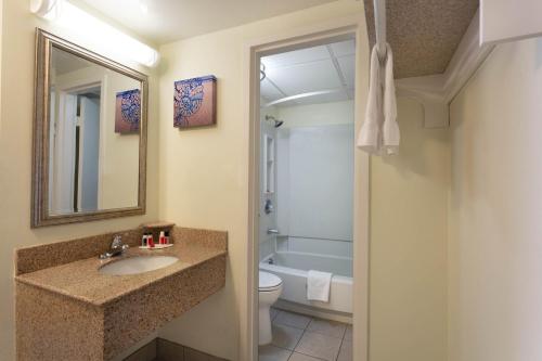 La salle de bains est pourvue d'un lavabo, de toilettes et d'un miroir. dans l'établissement Ramada Plaza by Wyndham Virginia Beach Oceanfront, à Virginia Beach