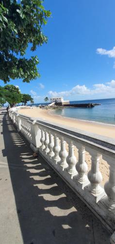 a white railing next to a beach with the ocean at Encantos do Porto da Barra in Salvador