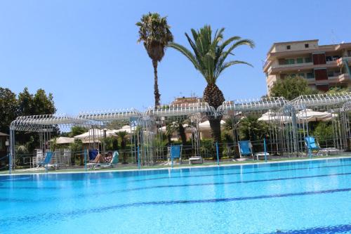a pool with chairs and palm trees next to a building at Hotel Mirasole International in Gaeta