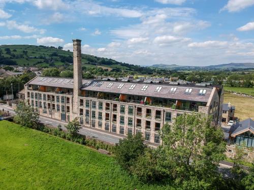 a large building with a chimney and a green field at The Works in Cononley