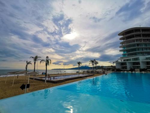 a large blue swimming pool next to a beach at Estudio 310 Nuevo Vallarta, frente al mar, totalmente equipado y amueblado! in Nuevo Vallarta 